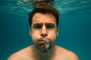 “Person holding their breath underwater, bubbles escaping as they try to stay submerged.”