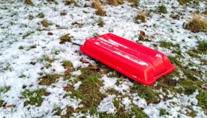 A red sled lying on patchy grass with a thin layer of snow, symbolizing mild disappointment in winter weather.