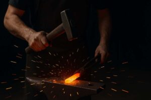 A blacksmith hammering a glowing piece of iron on an anvil, sparks flying into the dark background.