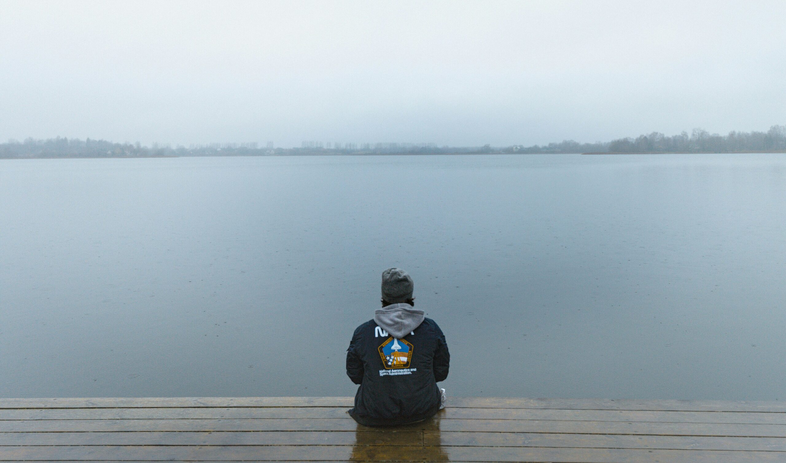 artem-balashevsky-Vx7ME85D4oU-unsplash - Low Two Pair A person sits quietly on a wooden dock at dawn, staring out at a calm lake and reflecting on life’s uncertainties.