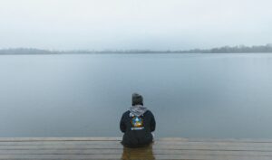 A person sits quietly on a wooden dock at dawn, staring out at a calm lake and reflecting on life’s uncertainties.