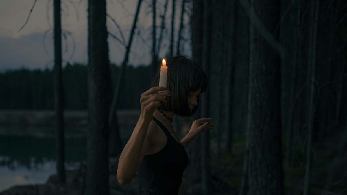 a woman carrying a candle into the woods