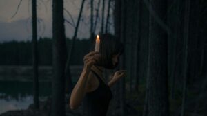 a woman carrying a candle into the woods