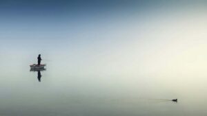 a person in a boat fishing alone on a flat pond