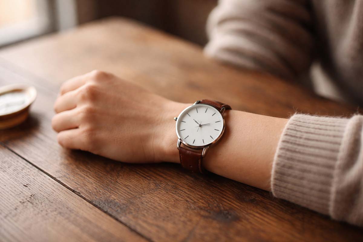 A watch worn on a wrist resting on a wooden table in soft natural light.